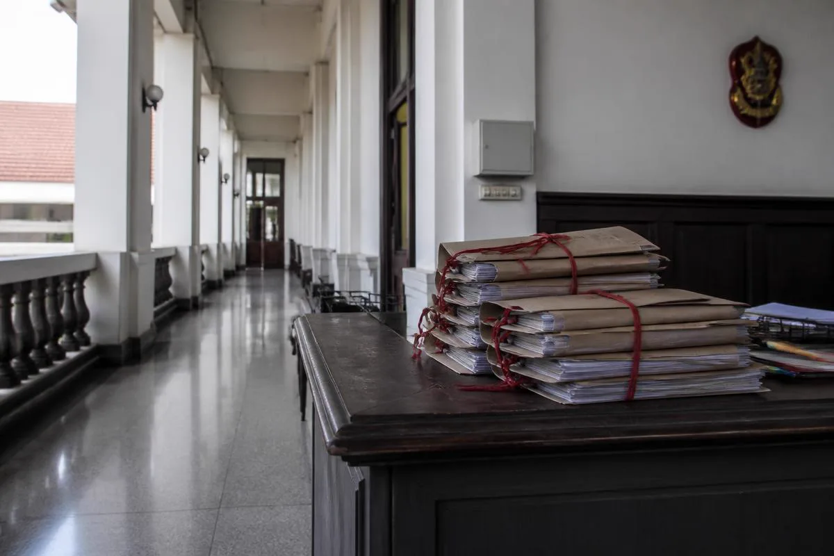 A Thai courthouse corridor with case files bound in red ribbon stacked on a clerk's counter